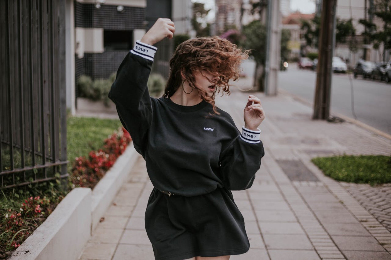 A woman in motion, dancing on an urban pavement in a fashionable outfit on a breezy day.