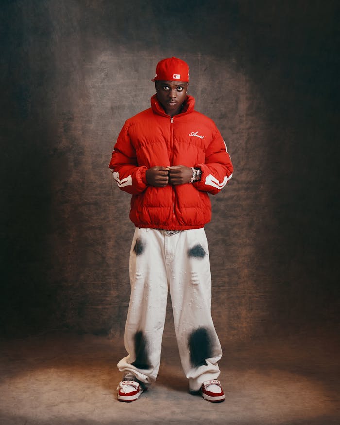 Stylish adult male posing in red urban jacket and cap in studio setting.